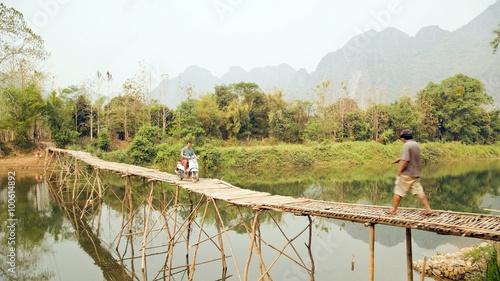 Cheerful Tourist crossing bamboo bridge motorbike, limestone view, laos photo