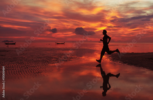 Fototapeta Naklejka Na Ścianę i Meble -   jogger on sunrise along the sand beach with mirror on the water