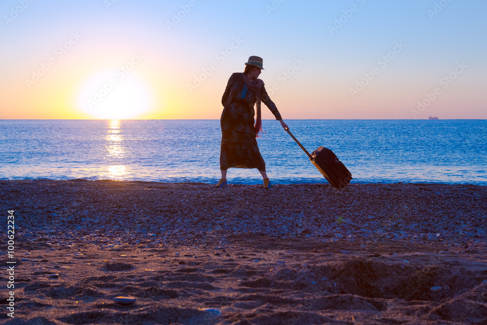 Silhouette of Lady walking along Sea Surf pulling Travel Suitcase