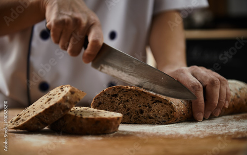 Woman chef cutting healthy bread with seeds on wooden board. Bakehouse. Bread production.