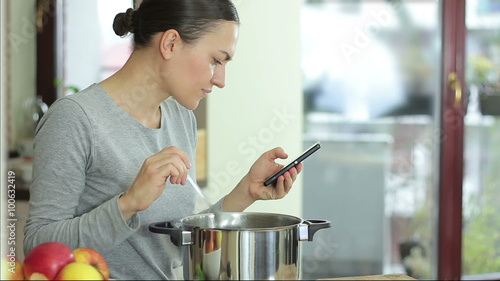 Brunette woman in kitchen following recipe on mobile phone