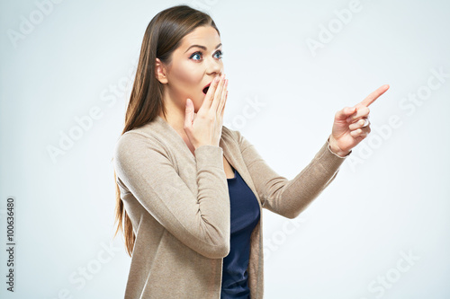 Young woman points  finger to the side, covering mouth in surpr photo