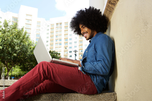 Smiling male student sitting outside working on laptop