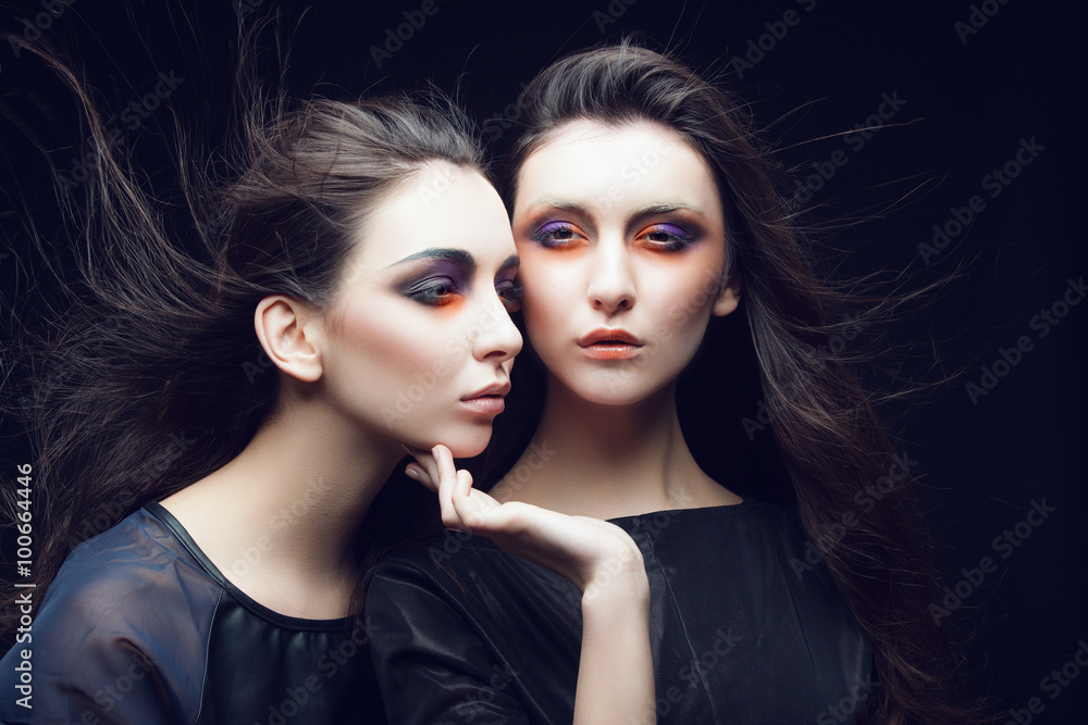 Obraz premium Portrait of two beautiful young girls twins in the studio with bright makeup on a black background, the concept of beauty