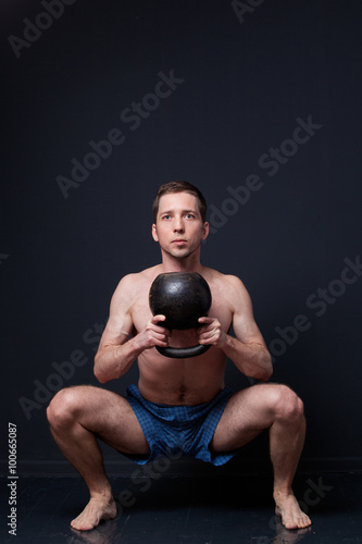 Young strong man in shorts doing squats with kettlebells in his