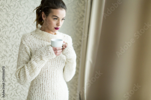 Pretty young woman with cup of coffee by the window