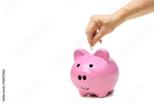 old female hand putting a golden coin into a pink piggy bank - saving for retirement concept