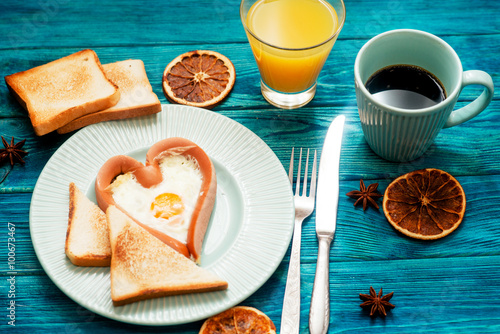 
romantic breakfast , heart-shaped fried eggs with sausage with toast, jam , hot black coffee , orange juice and spices on a wooden background