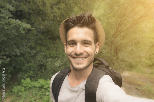 Handsome guy is taking a selfie with his smartphone in the nature - people, technology and lifestle concept