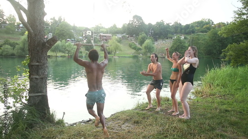 Handsome african american man jumping off rope swing into river while happy friends cheer for him