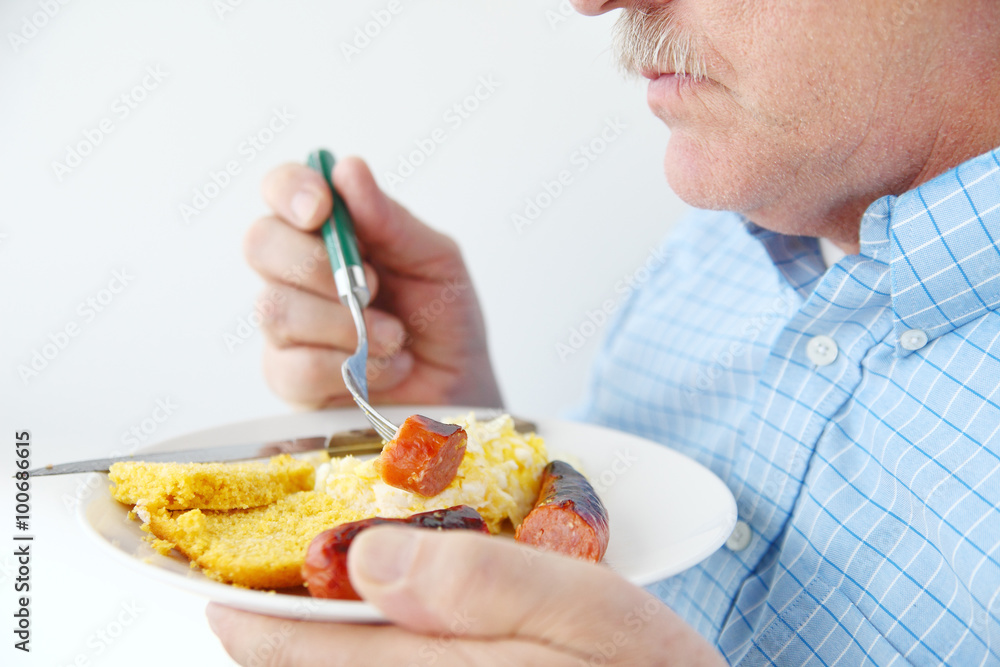 A man eating sausage, scrambled eggs and cornbread for breakfast