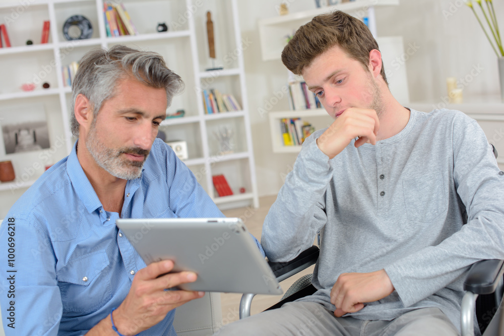 Man showing computer to younger man in wheelchair Man showing computer to younger man in wheelchair
