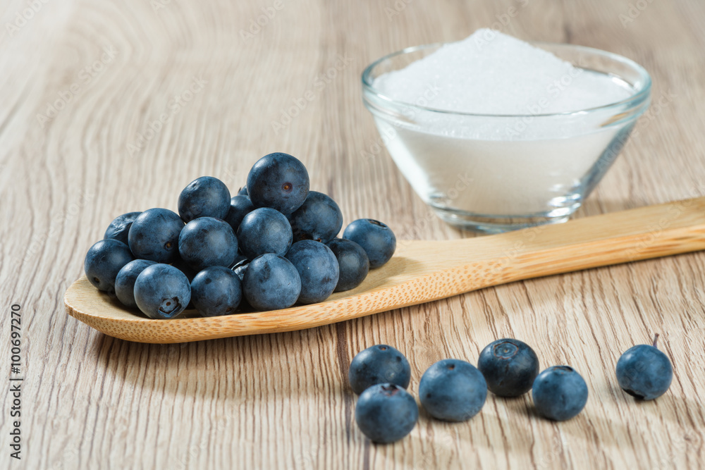 Wooden spoon with blueberries and glass bowl with sugar Wooden spoon with blueberries and glass bowl with sugar