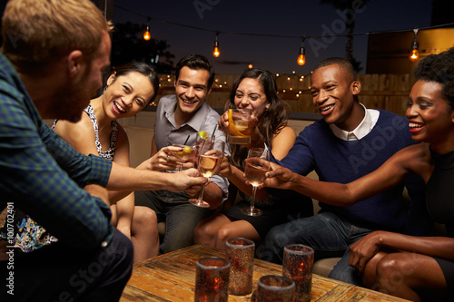 Group Of Friends Enjoying Night Out At Rooftop Bar