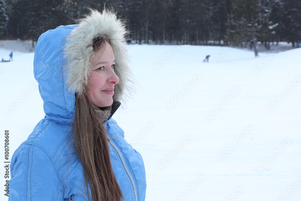 The beautiful woman with long hair in a blue jacket with a hood against snow and the wood in the winter
The beautiful woman with long hair in a blue jacket with a hood against snow and the wood in the winter