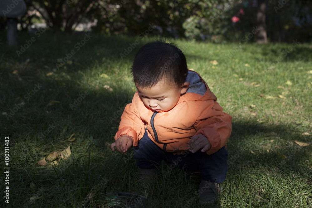 Cute Chinese baby boy studying a fountain blow hole in grass Cute Chinese baby boy studying a fountain blow hole in grass