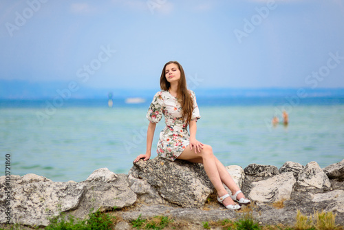 Beautiful woman sitting on rock over sea