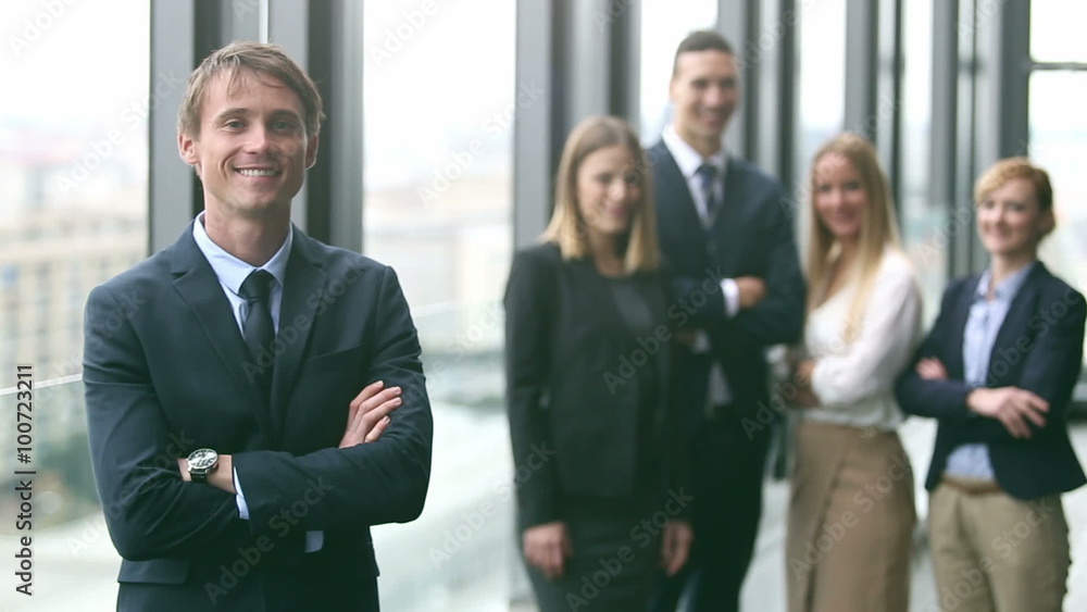 Portrait of handsome businessman smiling, colleagues in background Portrait of handsome businessman smiling, colleagues in background