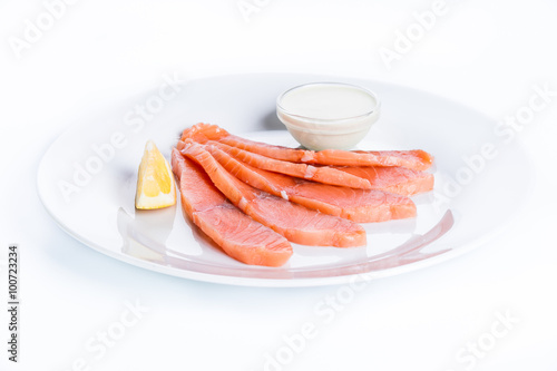 Thin slices of salmon fillet with lemon and sauce on a white bac
