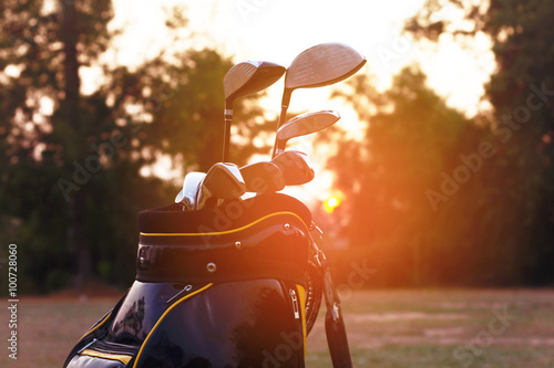 Golf clubs in golf bag on golf field at sunset