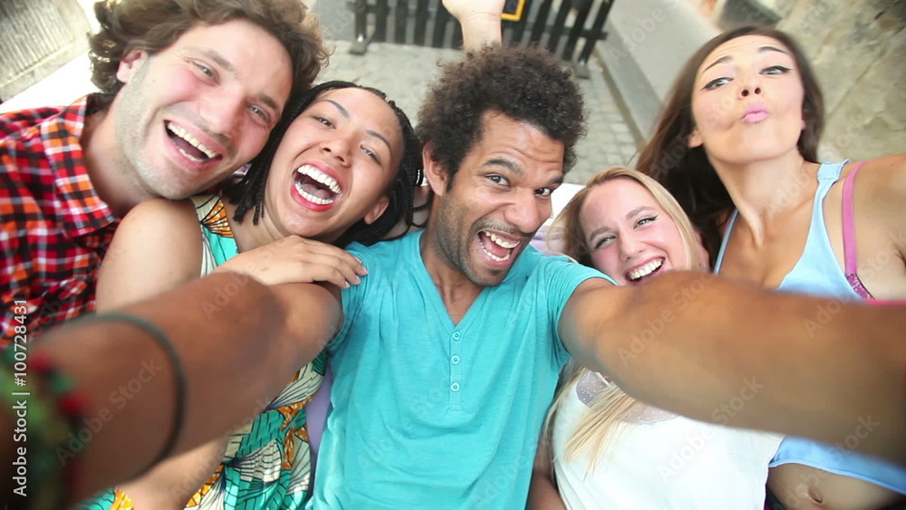 Five young adults laughing while taking a group selfie Five young adults laughing while taking a group selfie
