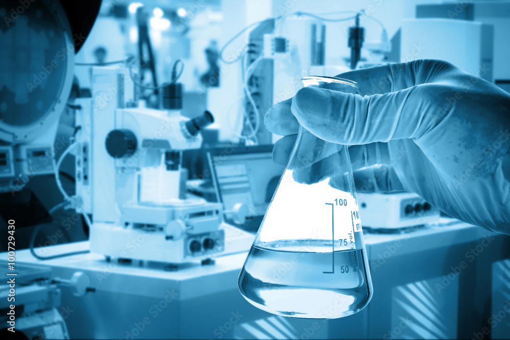 Flask in scientist hand with lab equipment background 