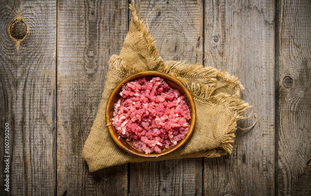 Raw minced meat in a wooden bowl on old fabric. Raw minced meat in a wooden bowl on old fabric.