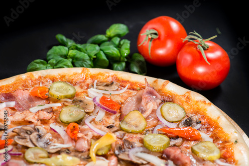 closeup Tasty pizza with tomatoes, cheese, basil and ham on a bl