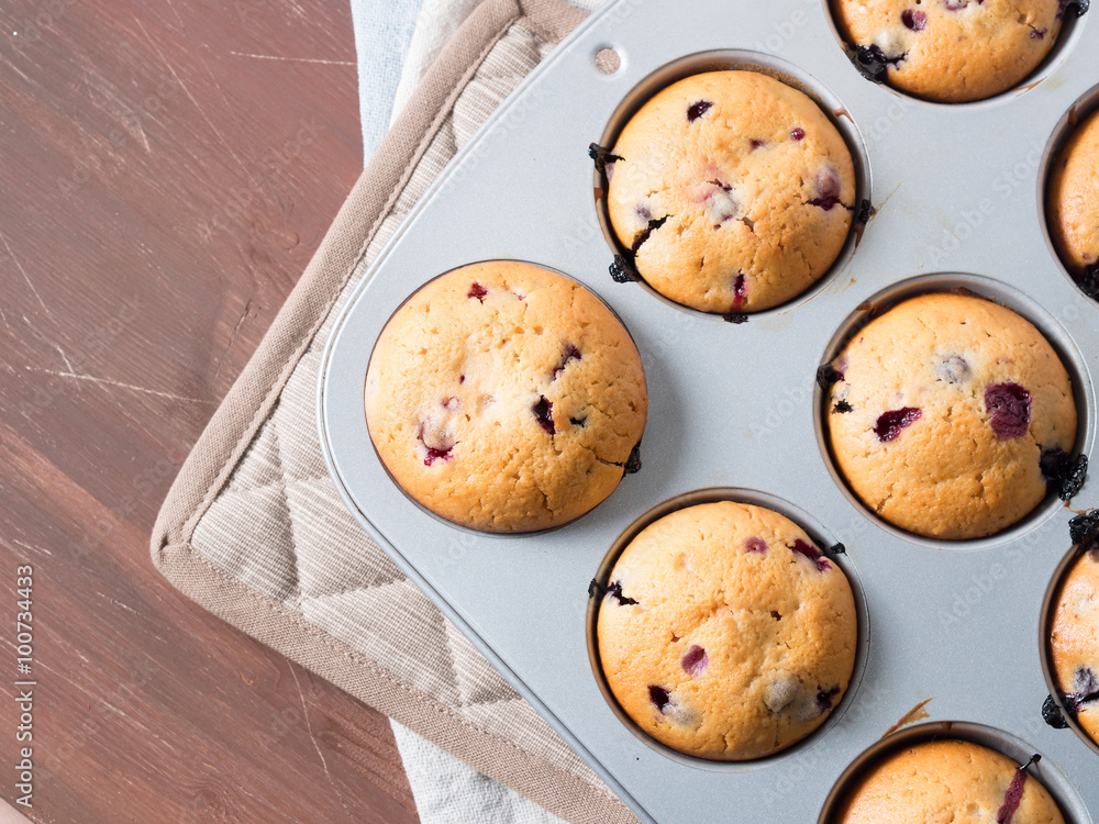 Just baked yogurt muffins with blackberries, blueberries and raspberries in a muffin tin on wooden table, top view closeup