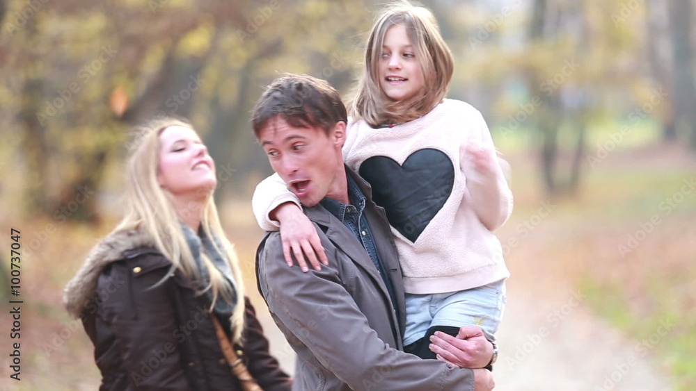 Family having fun in park, father carries daughter in his arms Family having fun in park, father carries daughter in his arms