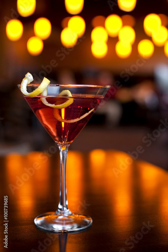 Cranberry martini in martini glass with lemon peel garnish and twinkling lights in the background.