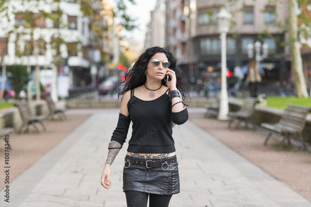 Tattooed woman with smart phone talking and walking in the street.