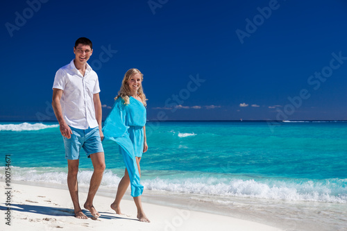 Happy couple walking on beach, smiling and looking at camera