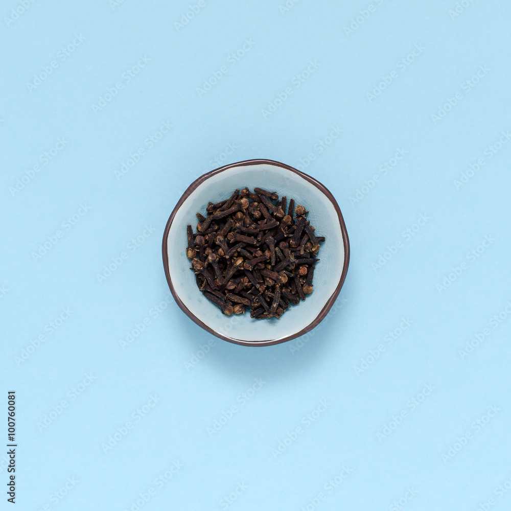 single spice bowl with cloves on turquoise background single spice bowl with cloves on turquoise background