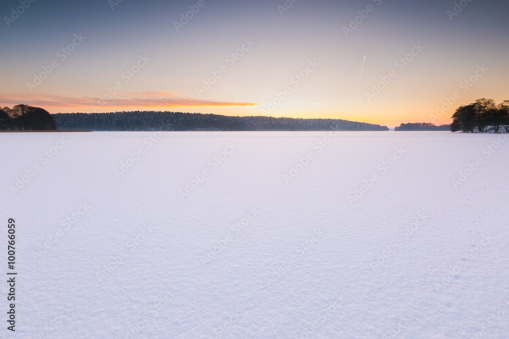 Sunset sky over frozen and snowy lake.