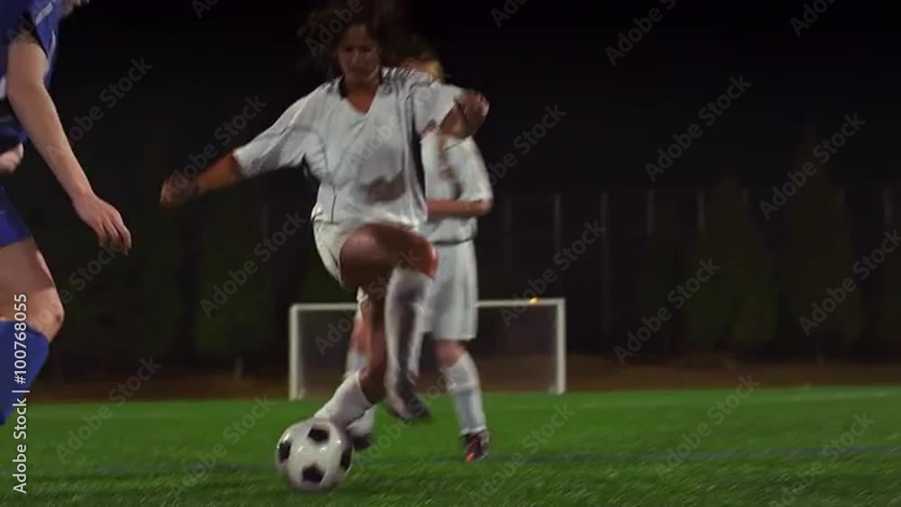 A female soccer player dribbles down the field during a game at night