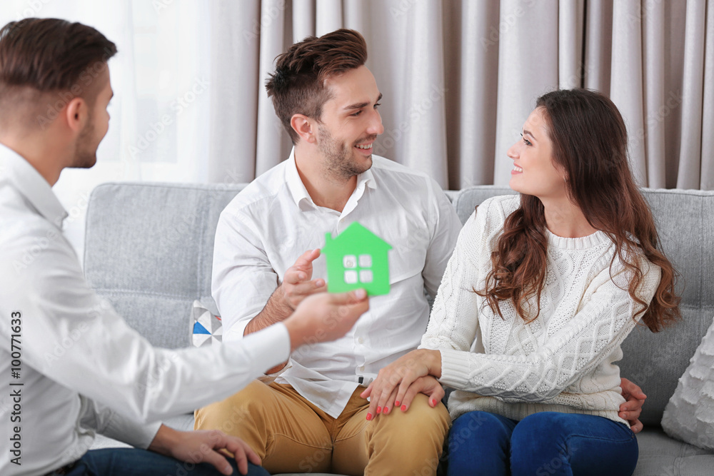 Estate agent with model of house and happy couple on home interior background Estate agent with model of house and happy couple on home interior background