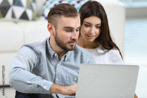 Happy couple sitting on the floor and working on laptop in a room © Africa Studio