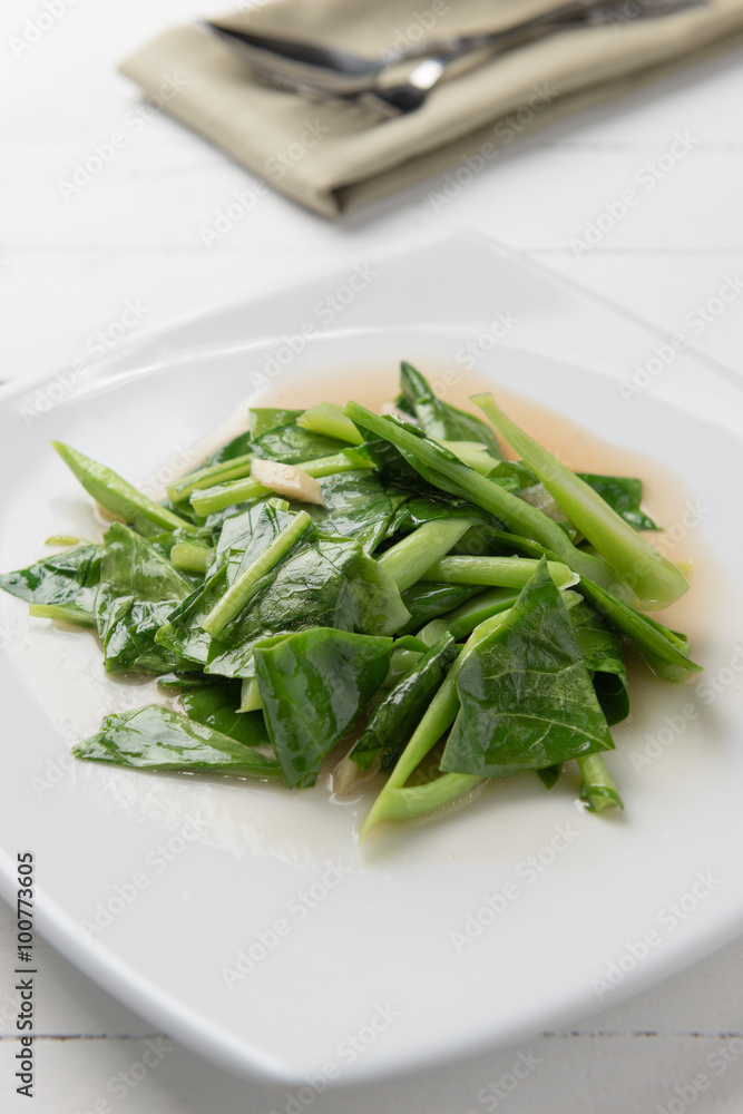 Kale stir fried in oyster sauce white plate on white table Kale stir fried in oyster sauce white plate on white table