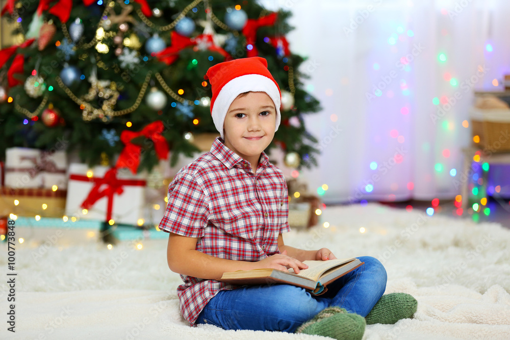 Cute small kid reading book on Christmas tree background Cute small kid reading book on Christmas tree background