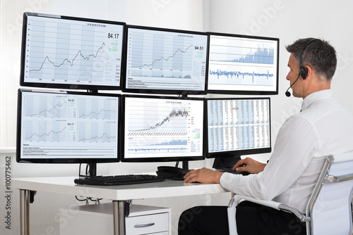 Stock Market Broker Looking At Graphs On Multiple Screens