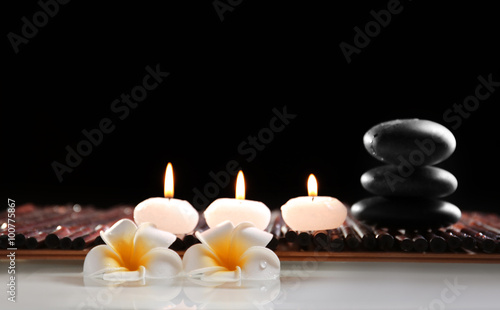 Spa still life with stones, candles and flowers in water on black background