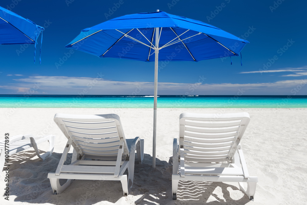 Caribbean beach with blue sun umbrellas and white beds