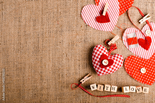 Sewing set: fabrics, threads, pins, buttons, tape, handmade hearts, words "with love" on cubes, burlap, sackcloth background. Retro design effects.