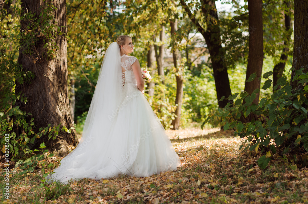 Fototapeta premium She is not lost. Beautiful young bride walking in the forest on a sunny wedding day