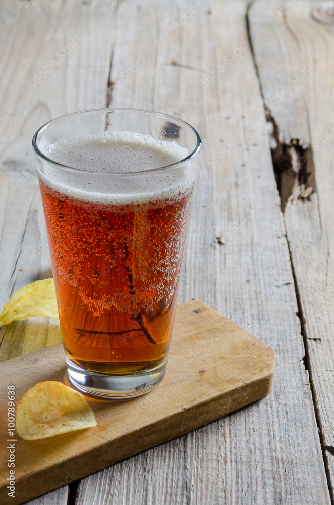 Beer into glass on wooden table with potato chips Beer into glass on wooden table with potato chips