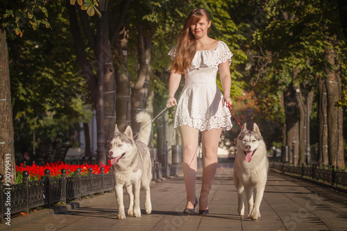 Young girl walking down the street with two dogs. A girl in a white dress. Siberian Huskies.