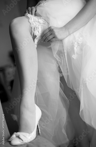 Невеста надевает кружевную подвязку ан ногу в туфельке с бантом и высоким каблуком