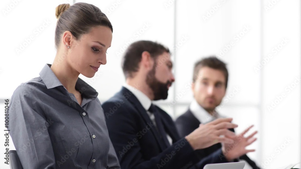 Business people having a meeting in the office and discussing together, a woman is smiling at camera in the foreground Business people having a meeting in the office and discussing together, a woman is smiling at camera in the foreground