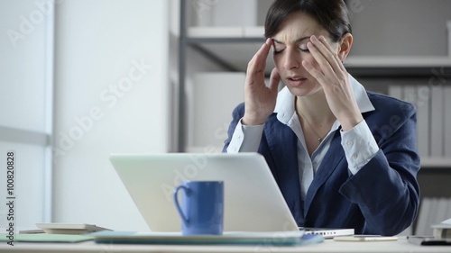 Tired bsuinesswoman working at office desk with a laptop, she is having an headache and touching her temples photo